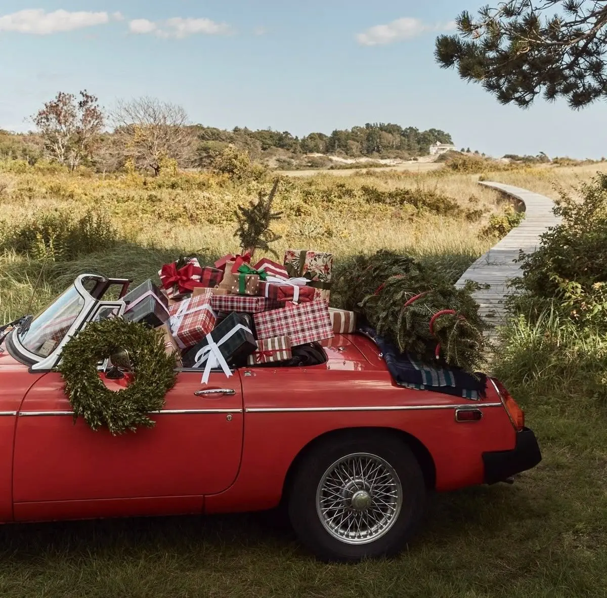 Vintage red convertible filled with wrapped Christmas gifts, wreaths, and evergreen trees